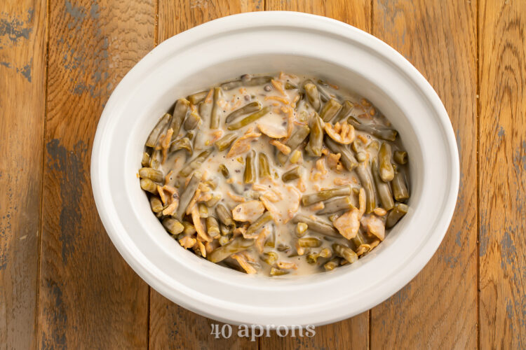 Overhead view of a Crockpot green bean casserole in a white ceramic slow cooker insert on a wooden table top.