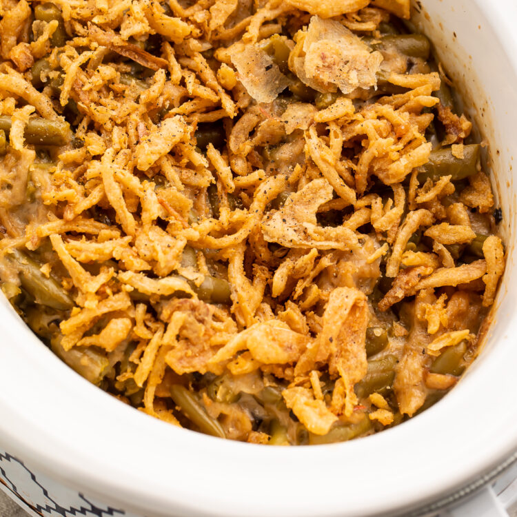 An overhead view of an angled oval Crockpot containing green bean casserole topped with crispy fried onions.