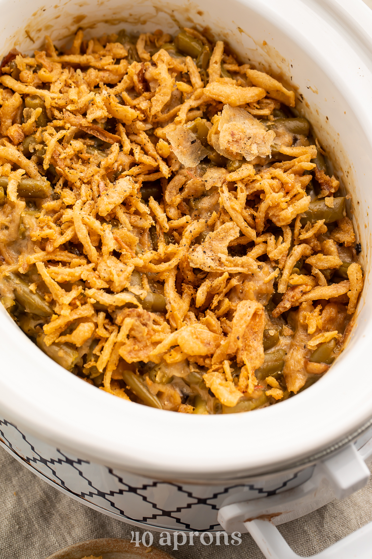 An overhead view of an angled oval Crockpot containing green bean casserole topped with crispy fried onions.
