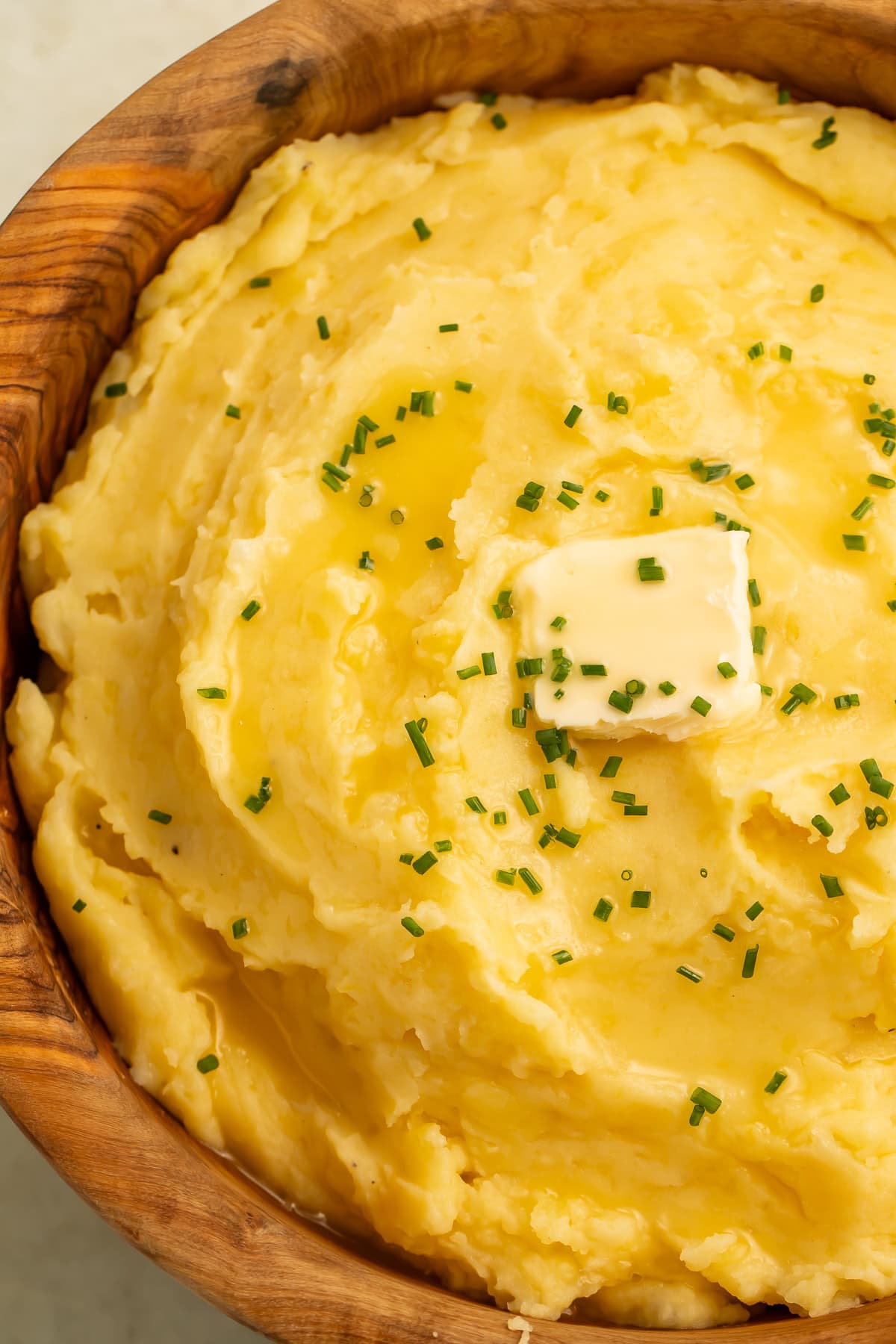 Wooden bowl of dairy free mashed potatoes topped with vegan butter.