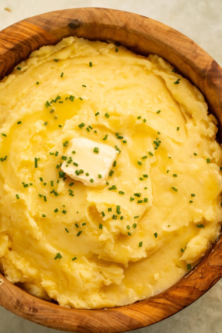 Close up of dairy free mashed potatoes topped with butter and chives in a wooden serving bowl.