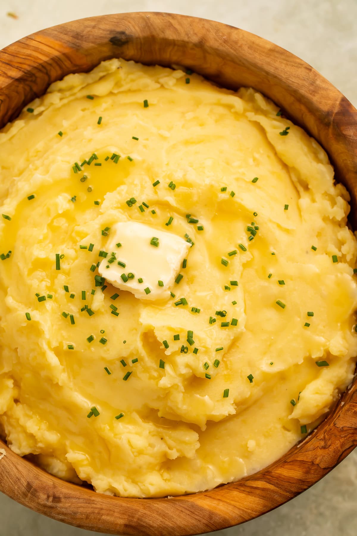 Close up of dairy free mashed potatoes topped with butter and chives in a wooden serving bowl.