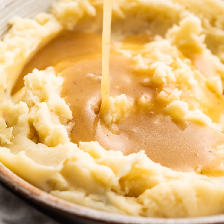 An angled look at a bowl of fluffy mashed potatoes with gluten free gravy being poured on top of the potatoes from above.