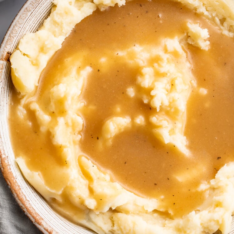 An overhead view of a bowl of fluffy mashed potatoes topped with a beautifully golden gluten-free gravy.