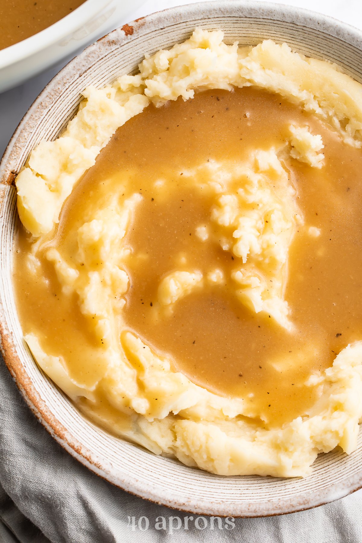 An overhead view of a bowl of fluffy mashed potatoes topped with a beautifully golden gluten-free gravy.