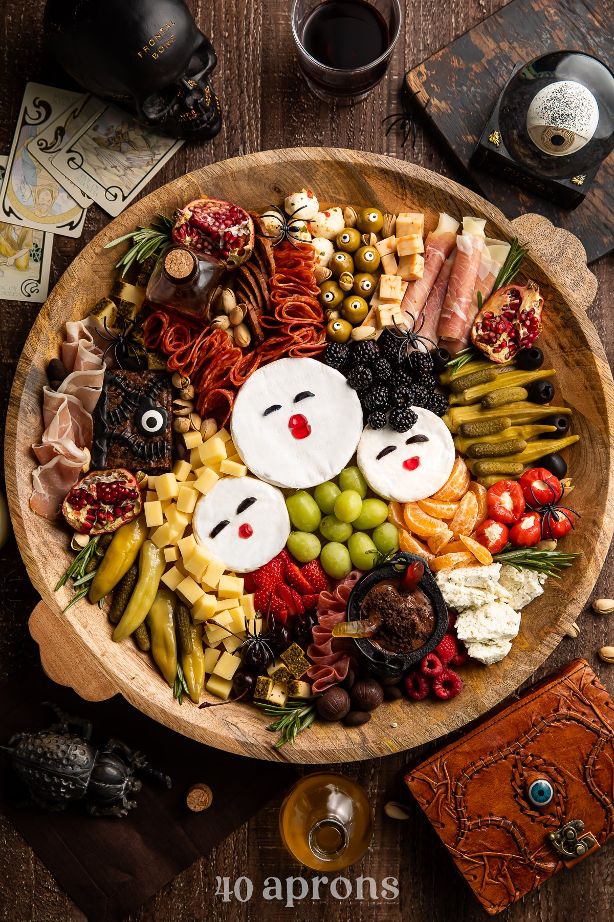 Overhead view of a Hocus Pocus themed charcuterie board with brie, fruit, cornichon, stuffed red peppers, marinated mozzarella, and other spooky snacks.