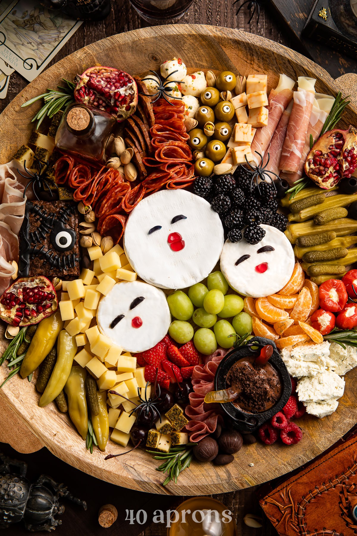 Overhead view of a Hocus Pocus themed charcuterie board with brie, fruit, cornichon, stuffed red peppers, marinated mozzarella, and other spooky snacks.