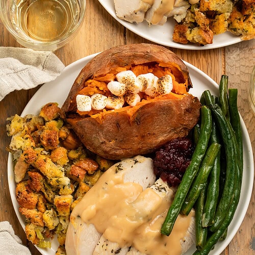 Thanksgiving dinner on a white plate with sliced turkey breast and gravy, green beans, stuffing, and a marshmallow-stuffed sweet potato.