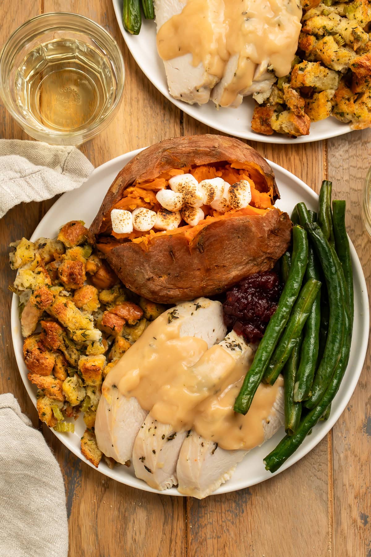 Thanksgiving dinner on a white plate with sliced turkey breast and gravy, green beans, stuffing, and a marshmallow-stuffed sweet potato.