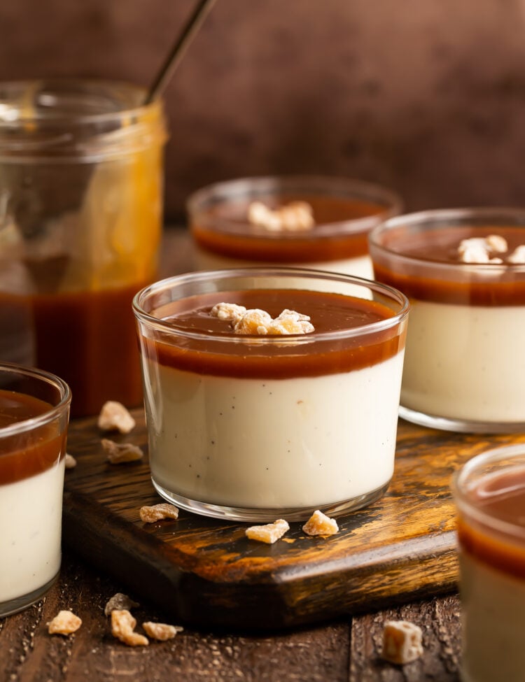 Side view of small glass pudding cups holding creamy panna cotta topped with rich caramel sauce.