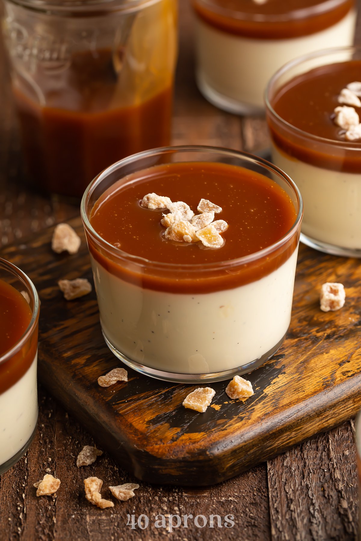 Overhead, angled view of vanilla bean panna cotta in a glass pudding cup topped with rich, dark caramel sauce.