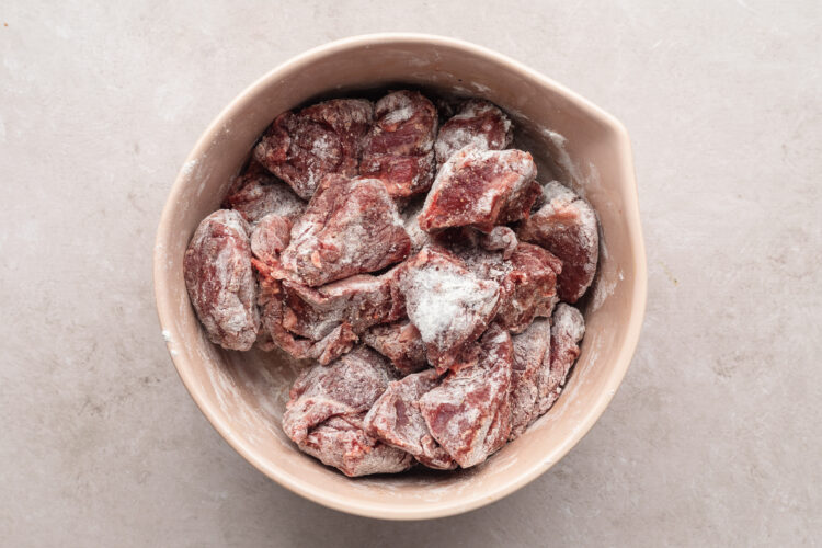 Overhead view of chunks of beef in a large bowl. Beef is liberally seasoned with salt.