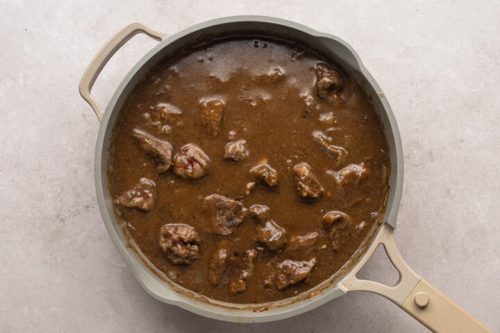 Overhead view of cooked beef tips in a pool of dark brown gravy in a large skillet.