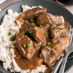Overhead view of beef tips and gravy plated with white rice on a dark shallow bowl.