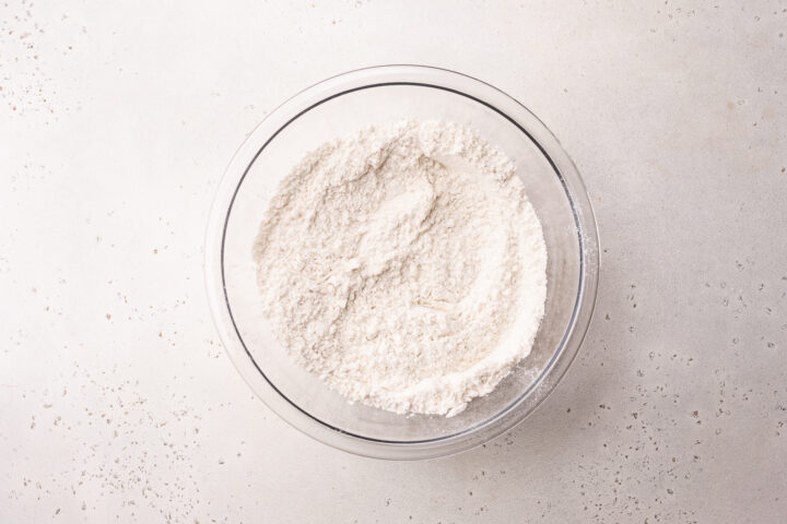 Overhead view of sifted flour in a glass mixing bowl.