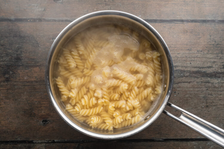 Overhead view of rotini pasta boiling in a large silver pot of water.