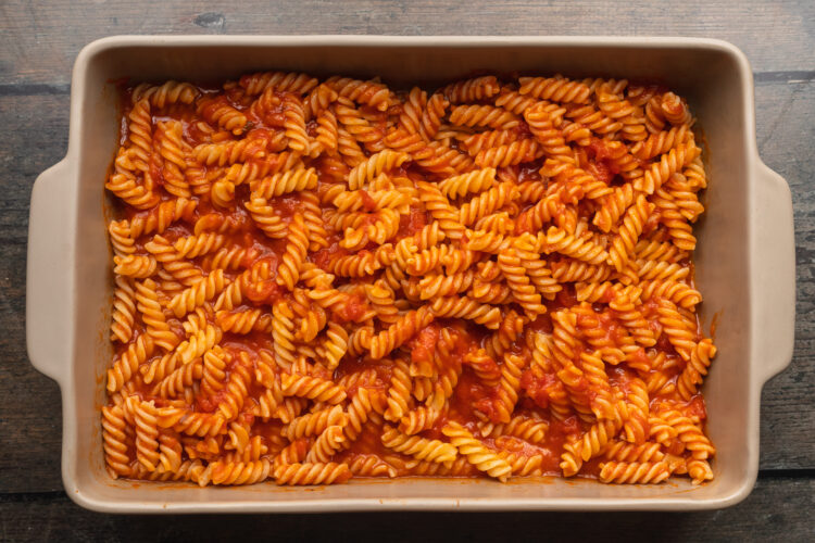 Overhead view of pasta and marinara sauce in a large rectangular baking dish.