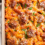 Overhead view of the corner of a large pan of meatball casserole with rotini pasta and cheese.