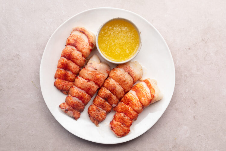 Overhead view of cooked sous vide lobster tails and lemon-garlic butter sauce on a white plate.