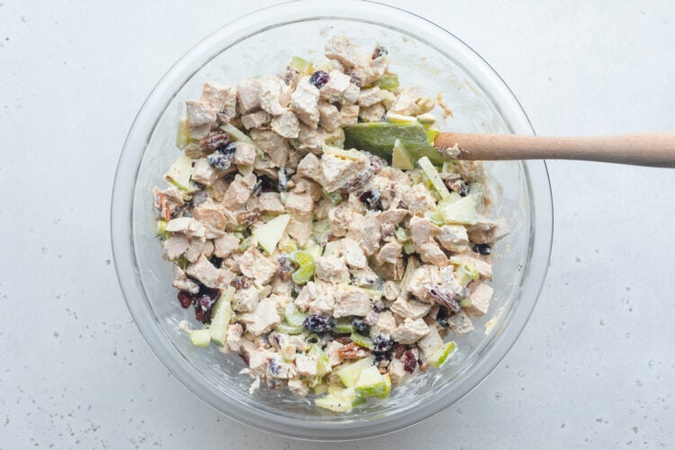 Overhead view of turkey salad in a large glass mixing bowl with a green spatula.