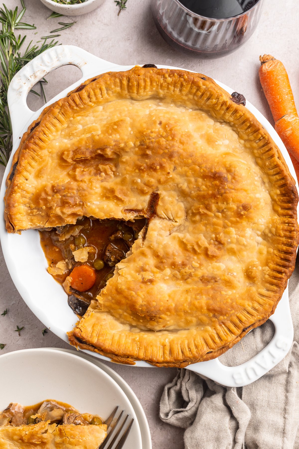 Overhead view of a beef pot pie with one wedge-shaped piece missing from the bottom left side of the pie dish.