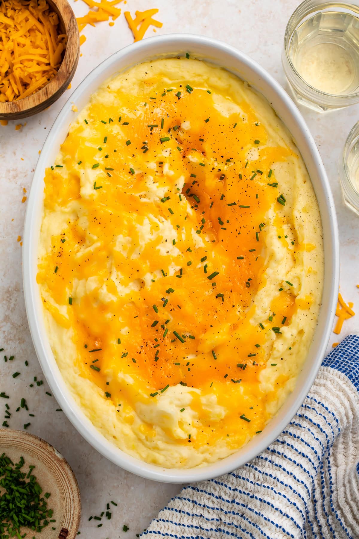 Oval serving dish of cheesy mashed potatoes scattered with chopped herbs.
