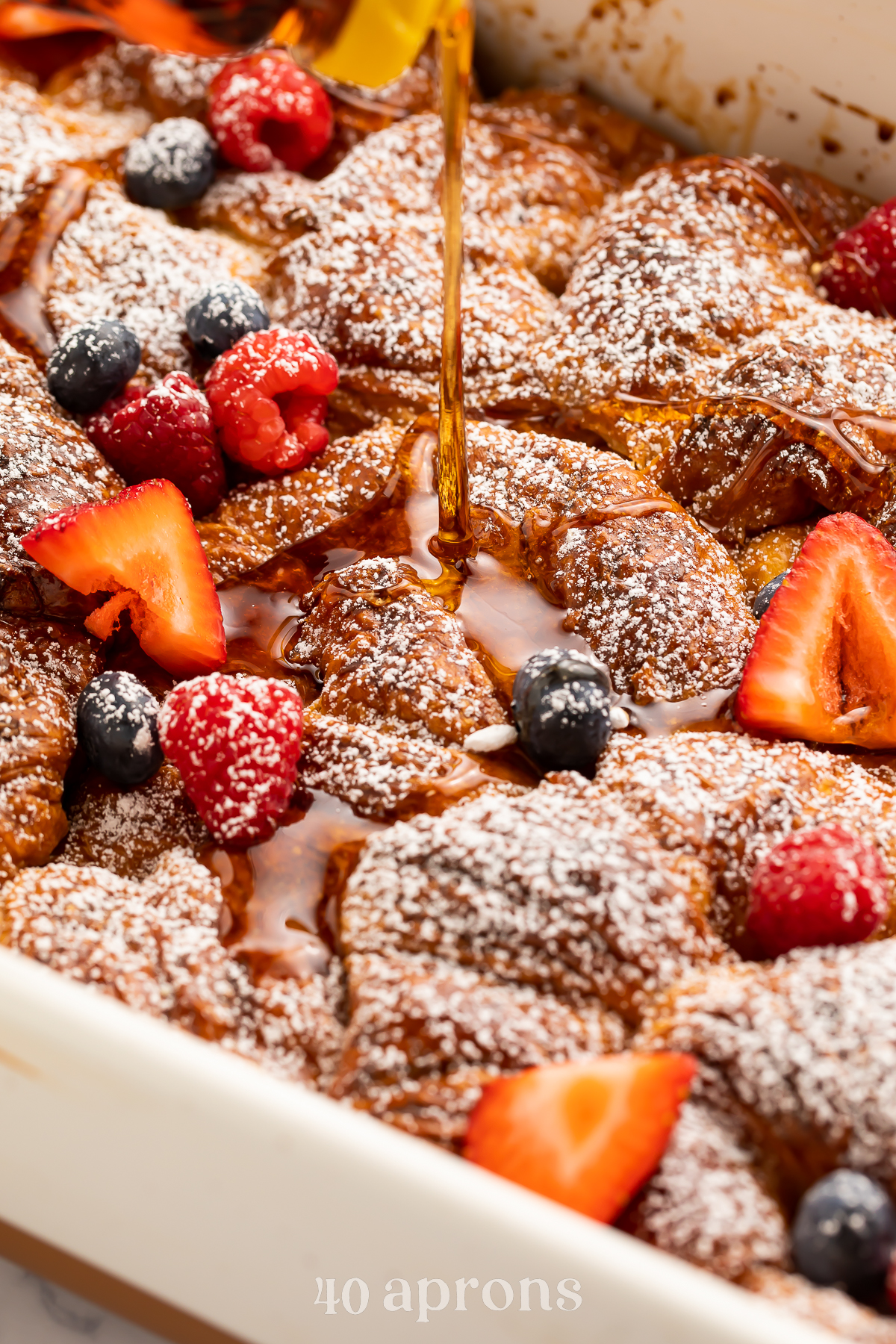 Close-up look at a croissant french toast casserole with brown sugar cinnamon in a casserole dish with strawberries and blueberries.