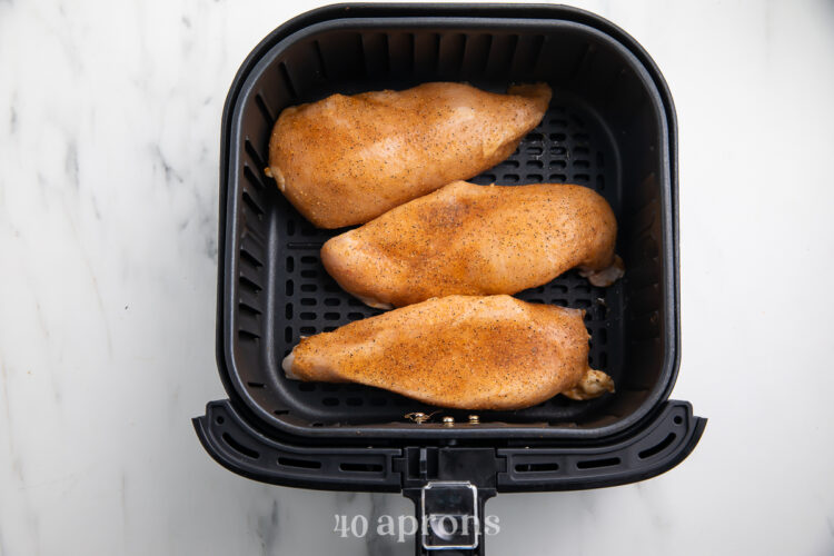Overhead view of 3 frozen, seasoned chicken breasts in an air fryer basket.