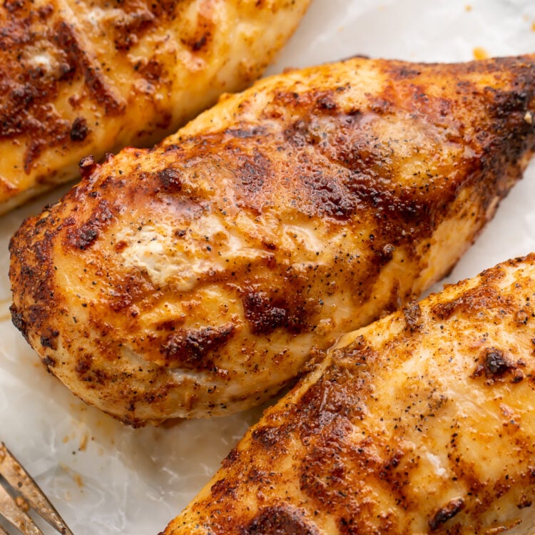 Overhead view of seasoned air fryer chicken breasts cooked from frozen lined up diagonally across a cutting board.