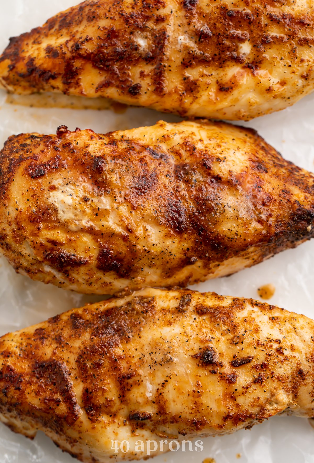 Overhead view of 3 frozen chicken breasts cooked in the air fryer and lined up next to each other on a cutting board.