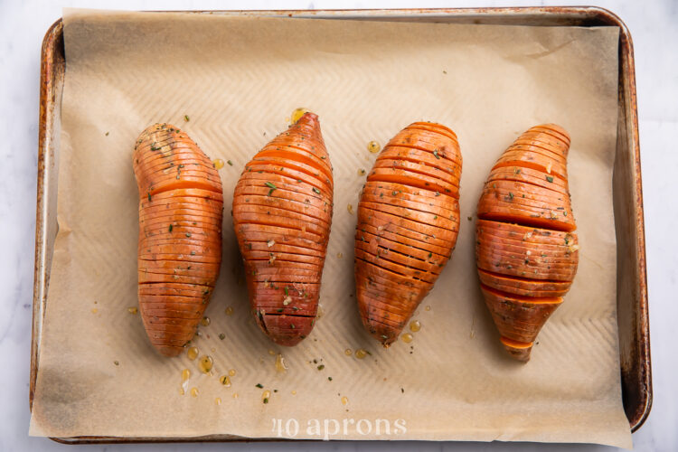 Overhead view of 4 thinly sliced hasselback sweet potatoes on a baking sheet lined with parchment paper.