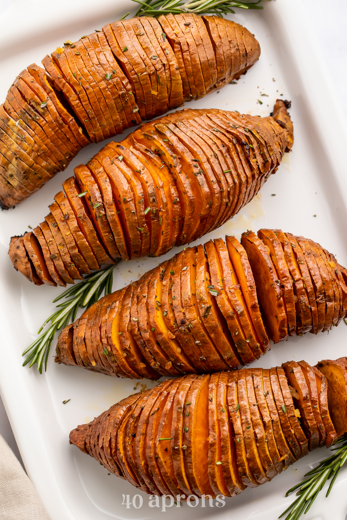 Overhead view of 4 hasselback sweet potatoes placed diagonally on a white rectangular serving tray.