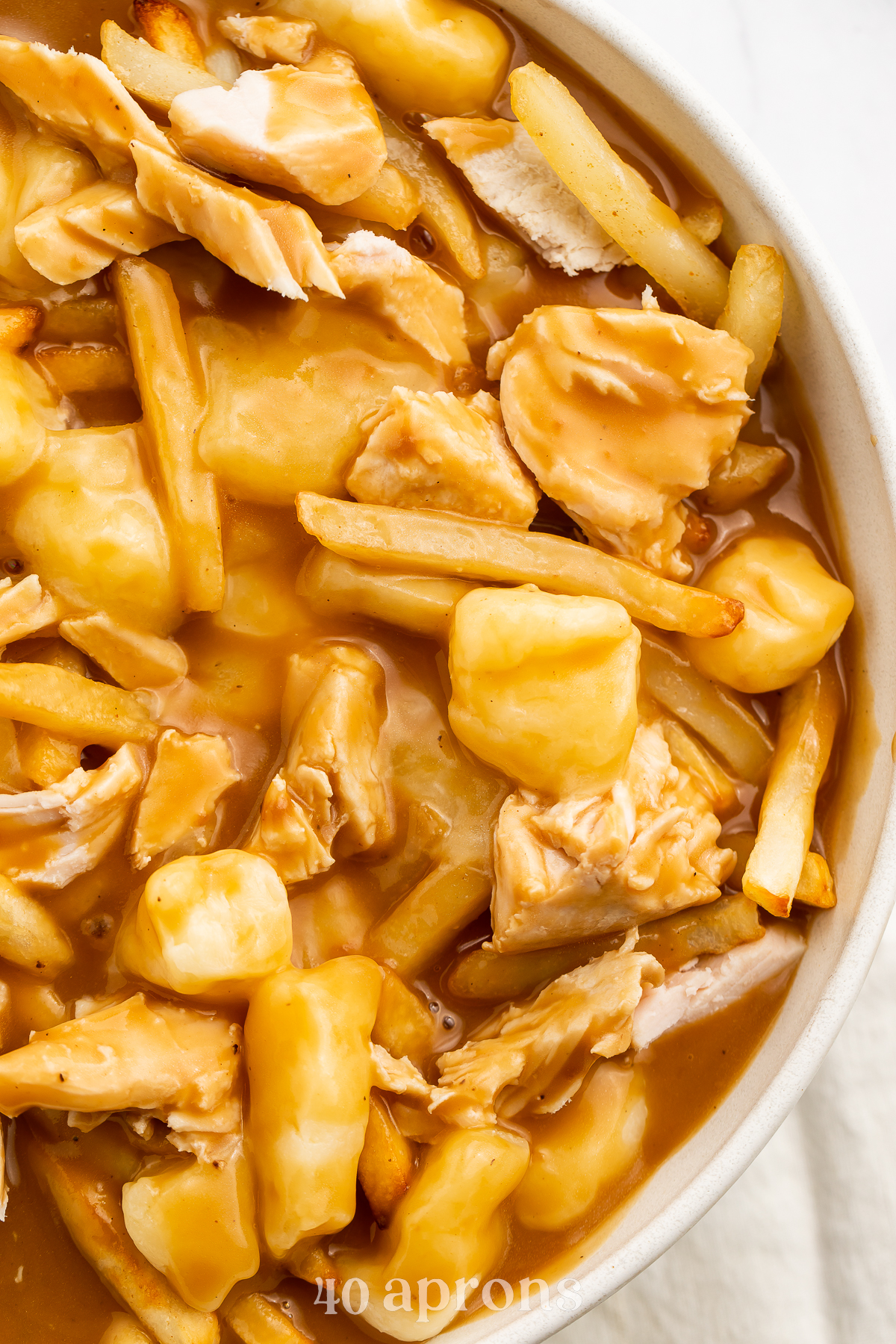 Overhead view of the right half of a large bowl of leftover turkey poutine with fries and gravy.
