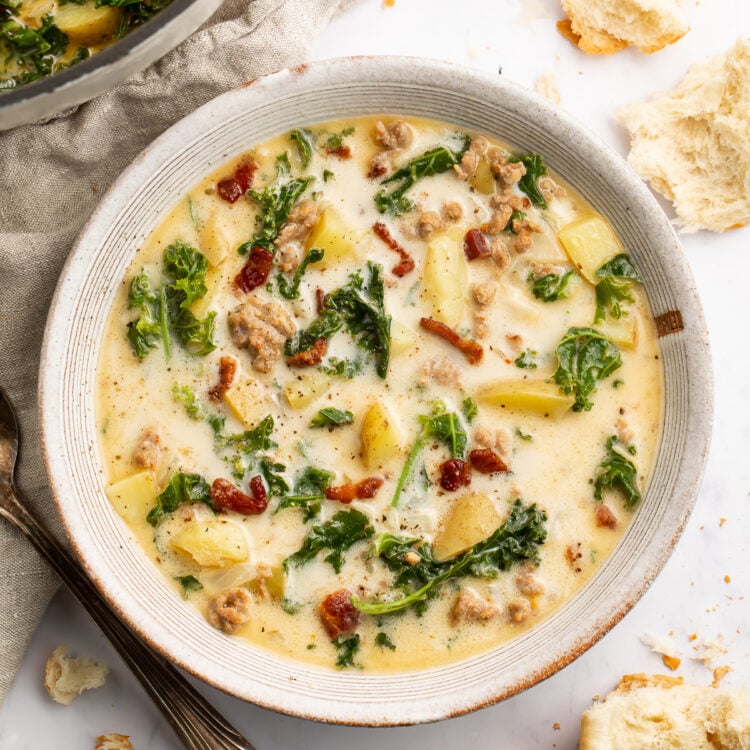 Overhead view of a white soup bowl holding Zuppa Toscana. Floating in the pale yellow soup are spinach, chopped bacon, and chunks of potatoes.