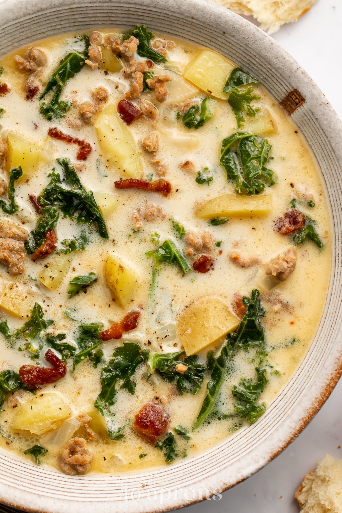 Close-up, overhead view of the right half of a bowl of zuppa toscana with kale, bacon, potatoes, and sausage.