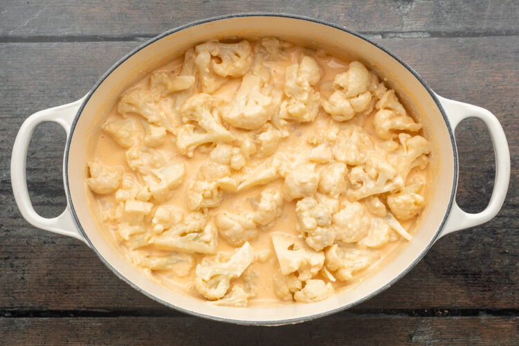 Overhead view of cauliflower florets covered in cheese sauce in a large, heavy-bottomed pot.