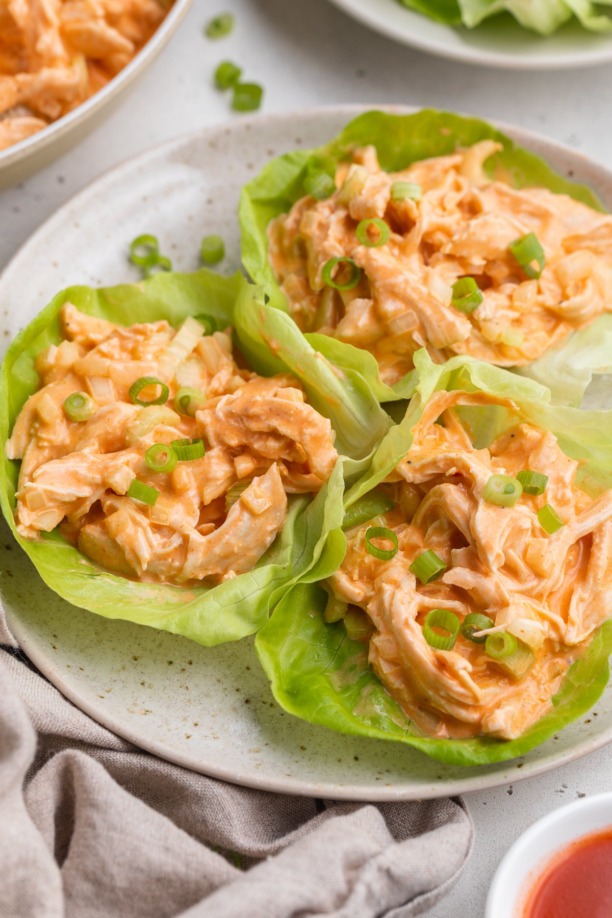 Whole30 buffalo chicken salad scooped into three iceberg lettuce cups on a white plate.
