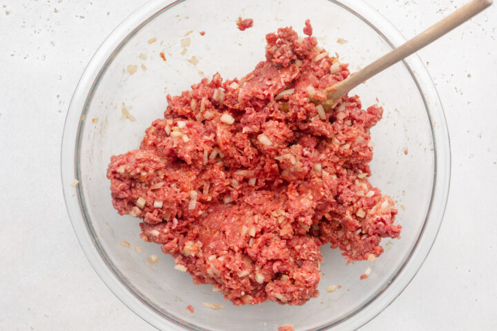 Mixture for Whole30 meatloaf in a large glass mixing bowl with a wooden spoon.
