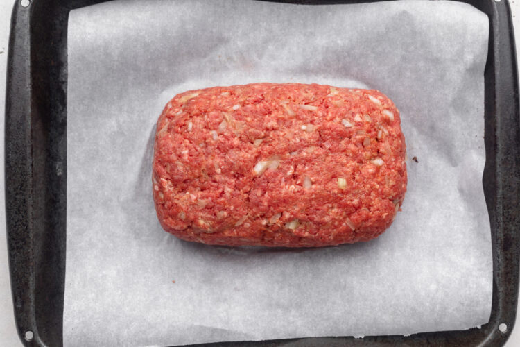 Uncooked, unglazed Whole30 meatloaf made with ground beef, shaped into a rectangular loaf in the center of a sheet pan covered in parchment paper.