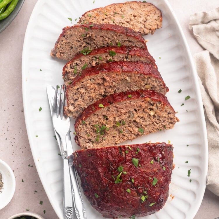 A Whole30 meatloaf, on a platter, sliced into 5 thin slices with a third of the loaf left whole.