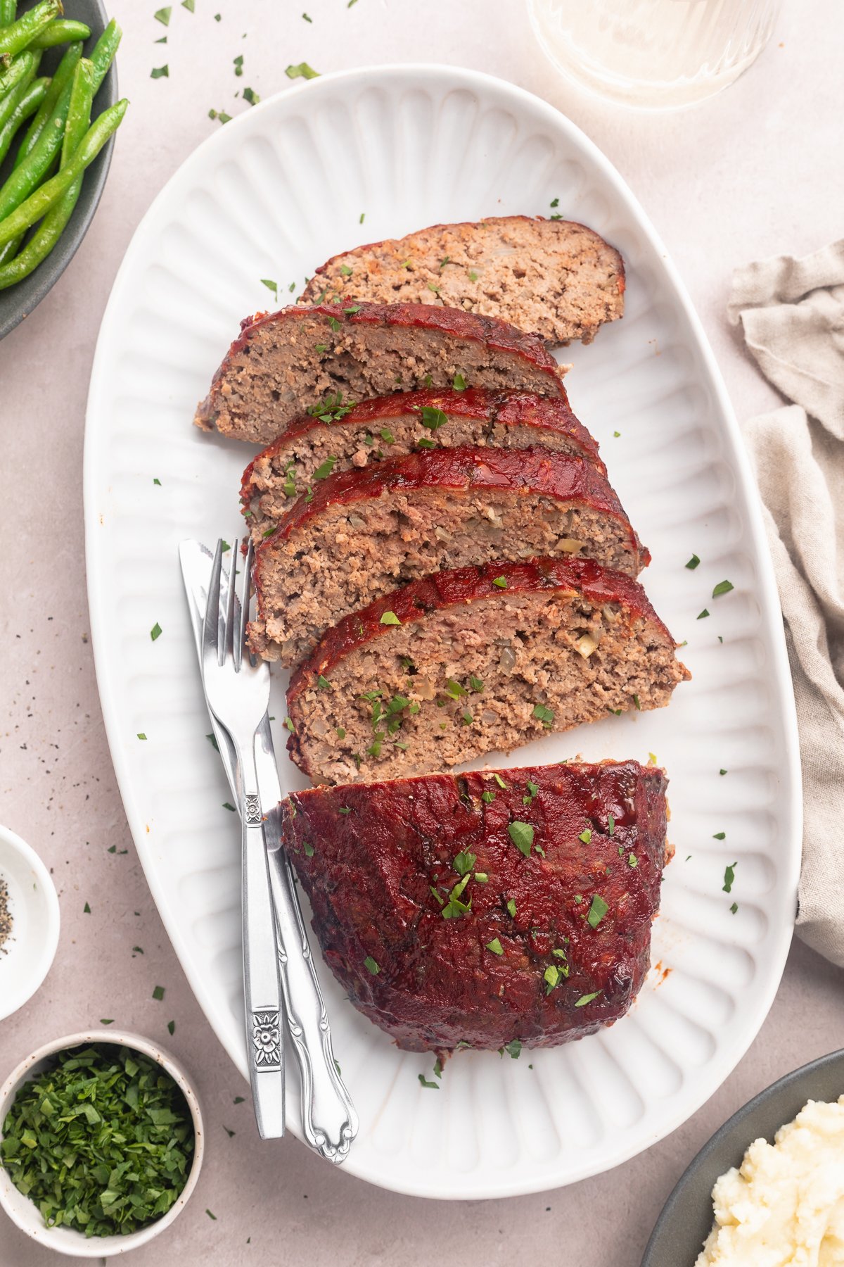A Whole30 meatloaf, on a platter, sliced into 5 thin slices with a third of the loaf left whole.