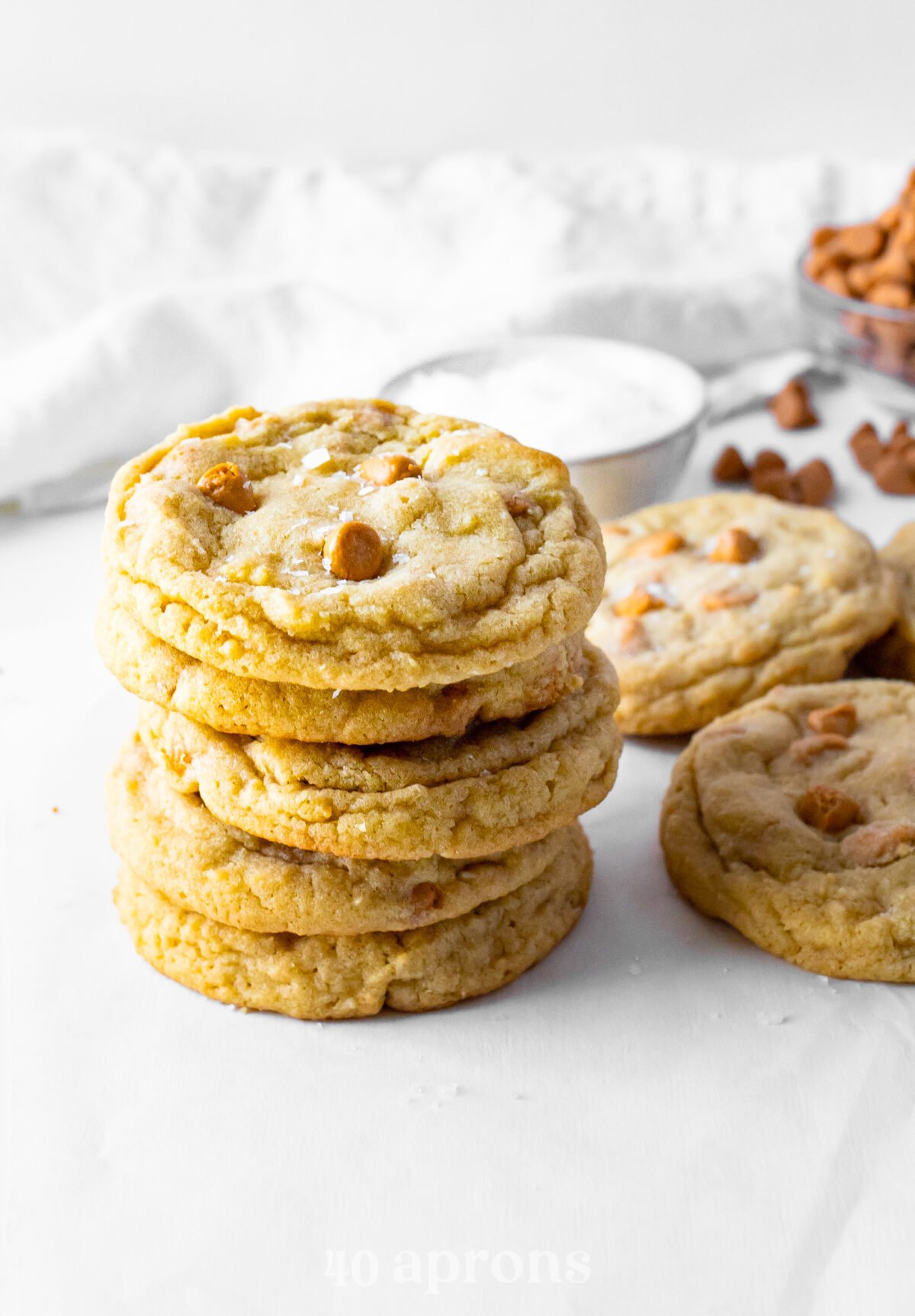 A side view of a stack of chewy butterscotch cookies next to a pile of cookies and in front of a napkin.
