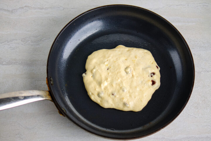 A single chocolate chip pancake cooking in the center of a medium skillet, just before being flipped over to cook top side.