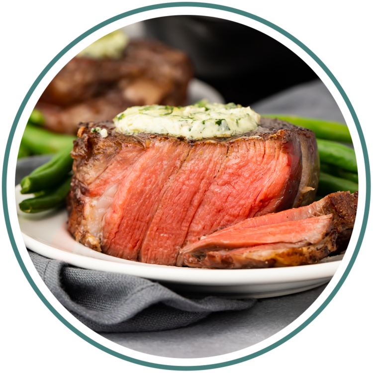 Reverse sear filet mignon topped with garlic herb butter, sitting on a white plate, cut to show medium-rare inside.