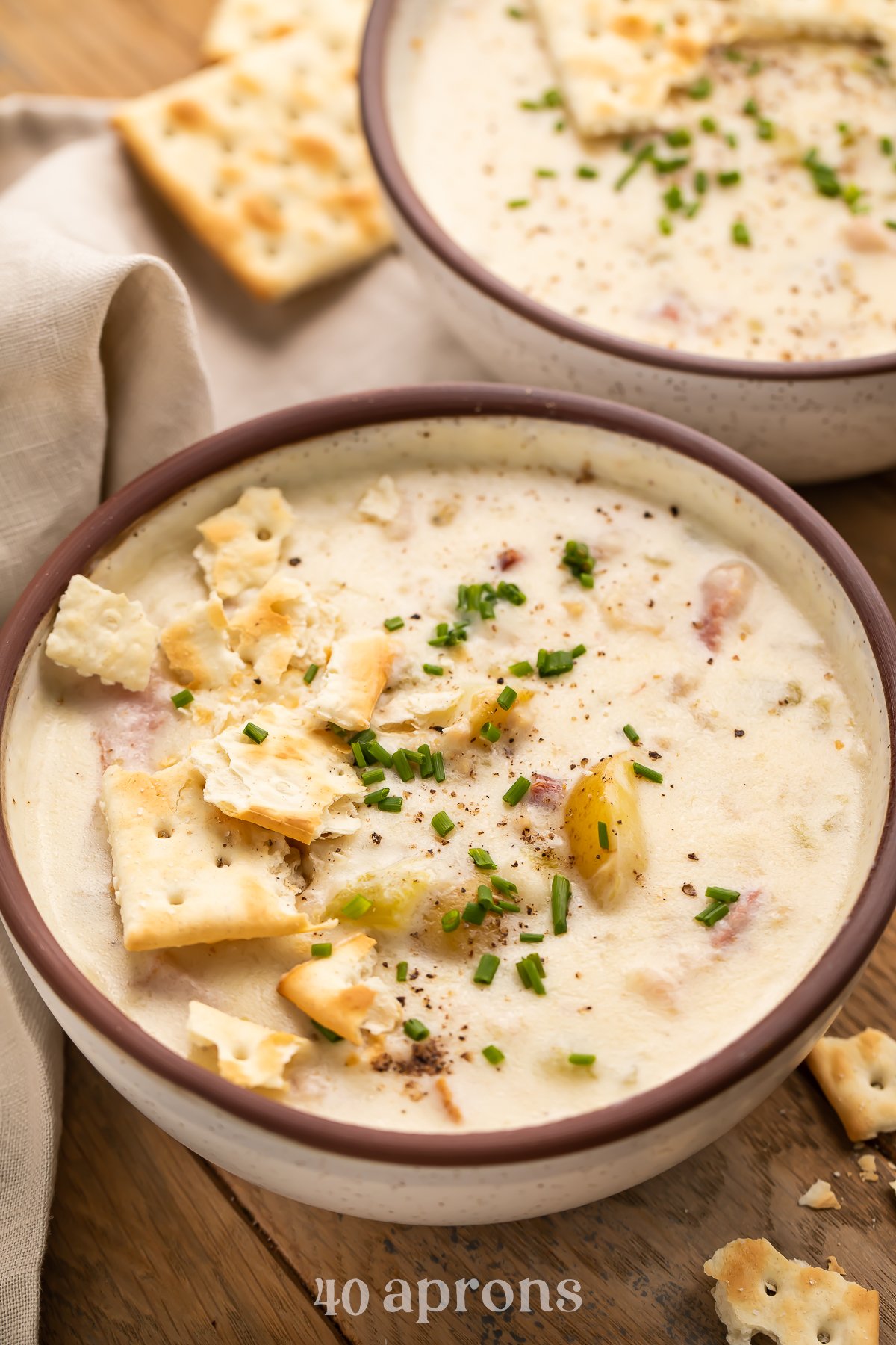 Angled overhead view of Instant Pot clam chowder in two rustic serving bowls on a wooden table with saltines.