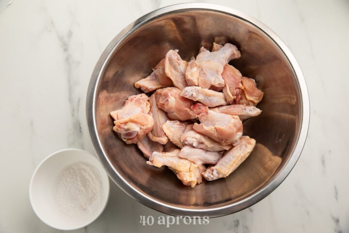 Overhead view of raw chicken wings in a large silver bowl, next to a Whole30 "breading" mixture in a small white bowl.