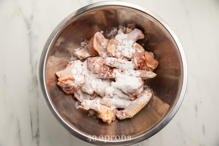 Overhead view of chicken wings topped with a Whole30 "breading" mixture in a large silver mixing bowl.