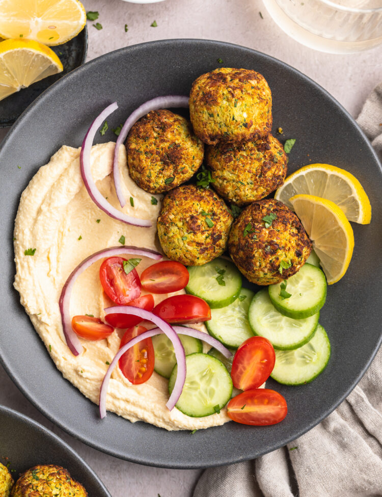 Overhead view of a bowl of air fryer falafel with a cucumber and tomato salad on a table with a napkin.