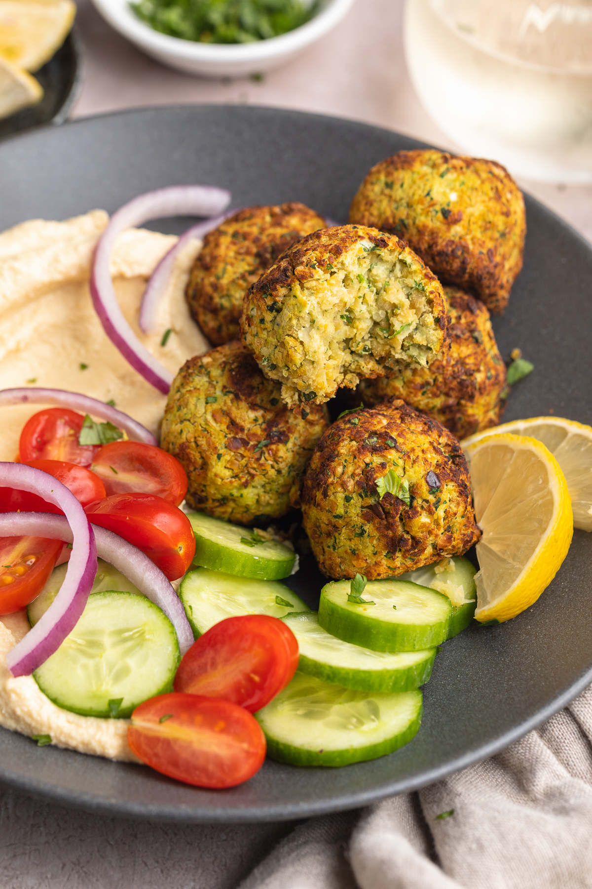 Overhead view of a bowl of air fryer falafel with a cucumber and tomato salad on a table with a napkin.