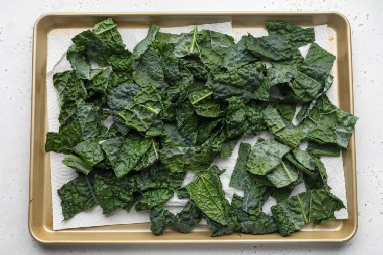 Rinsed kale leaves laying on paper towels on a baking sheet to dry.